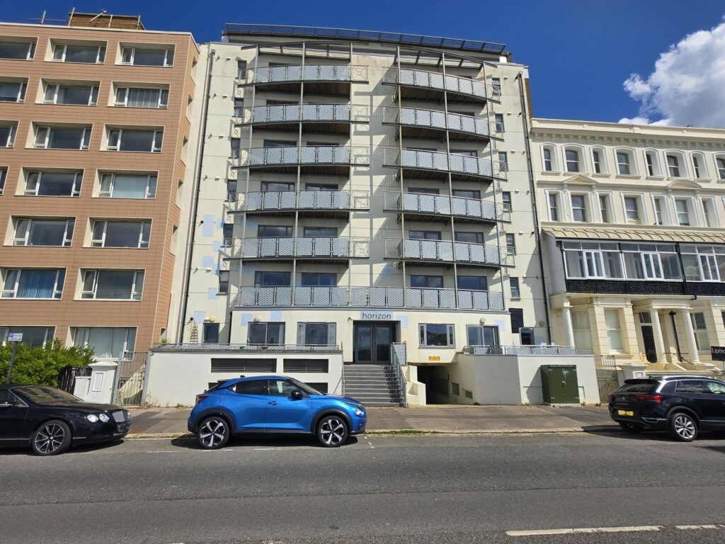 Multi-storey residential building with balconies and decorative metal railings viewed from the street.